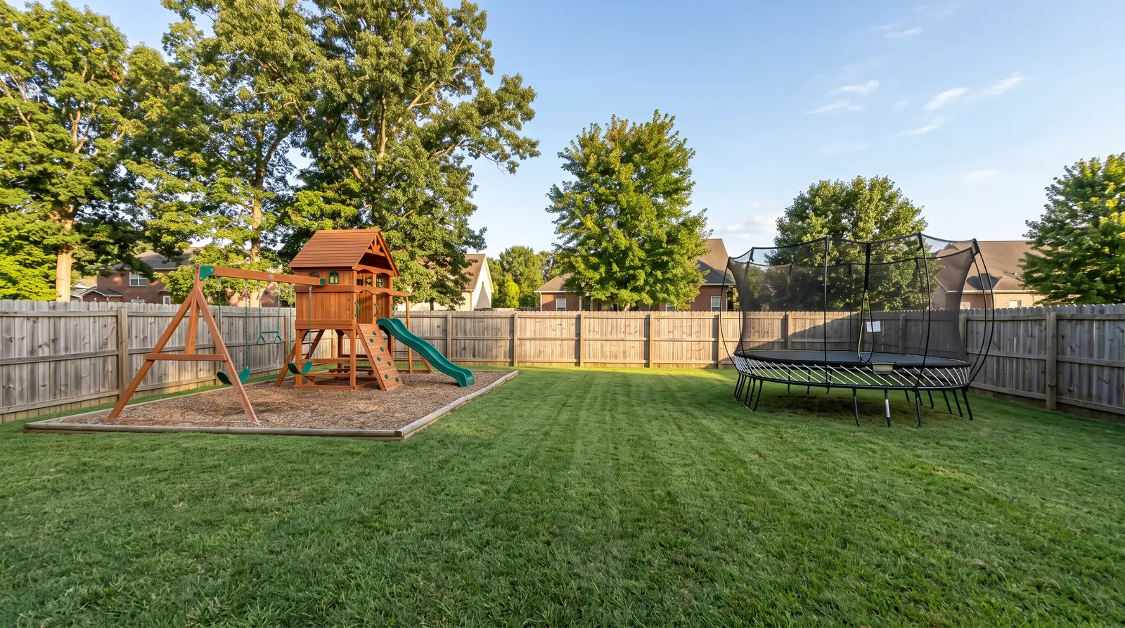 A well-kept suburban Middle Tennessee backyard in the afternoon with a cedar playset, a round trampoline with a safety net and a wooden privacy fence, tidy lawn and blue sky