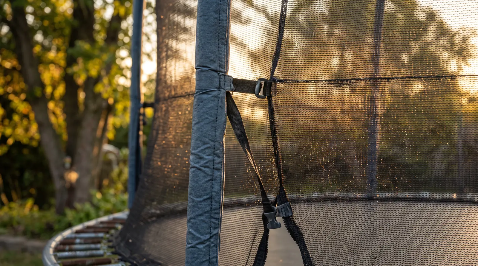 A close-up of a trampoline safety net enclosure with padded poles and the mesh net, golden light behind, shallow depth of field